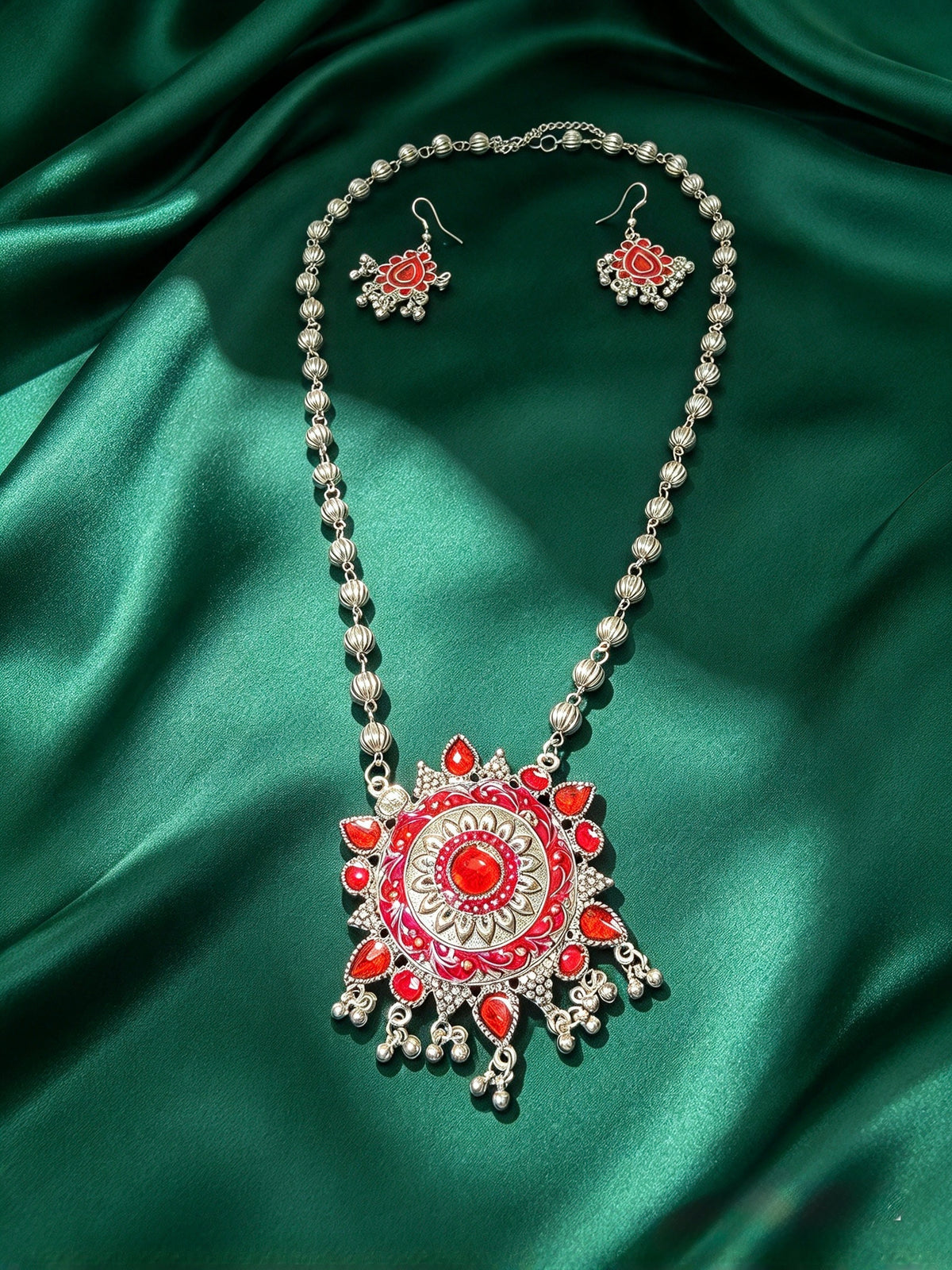 Mohe Rang Do Laal necklace and earrings laid on green satin, showing the red enamel pendant, dangling beads and extension chain