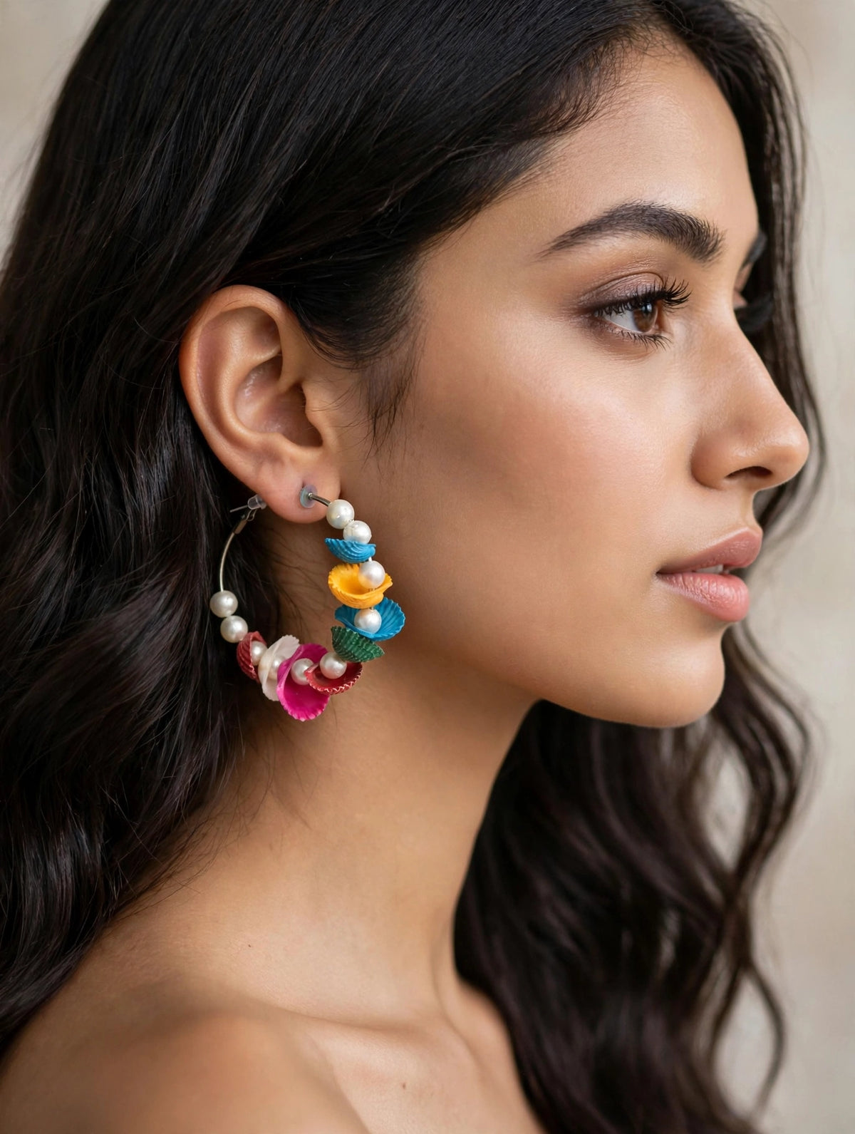 Multicolour shell-shaped hoop earrings with faux pearls worn by a model.