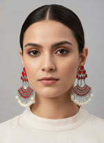 Display of ornate earrings with red and white stones on a stand.