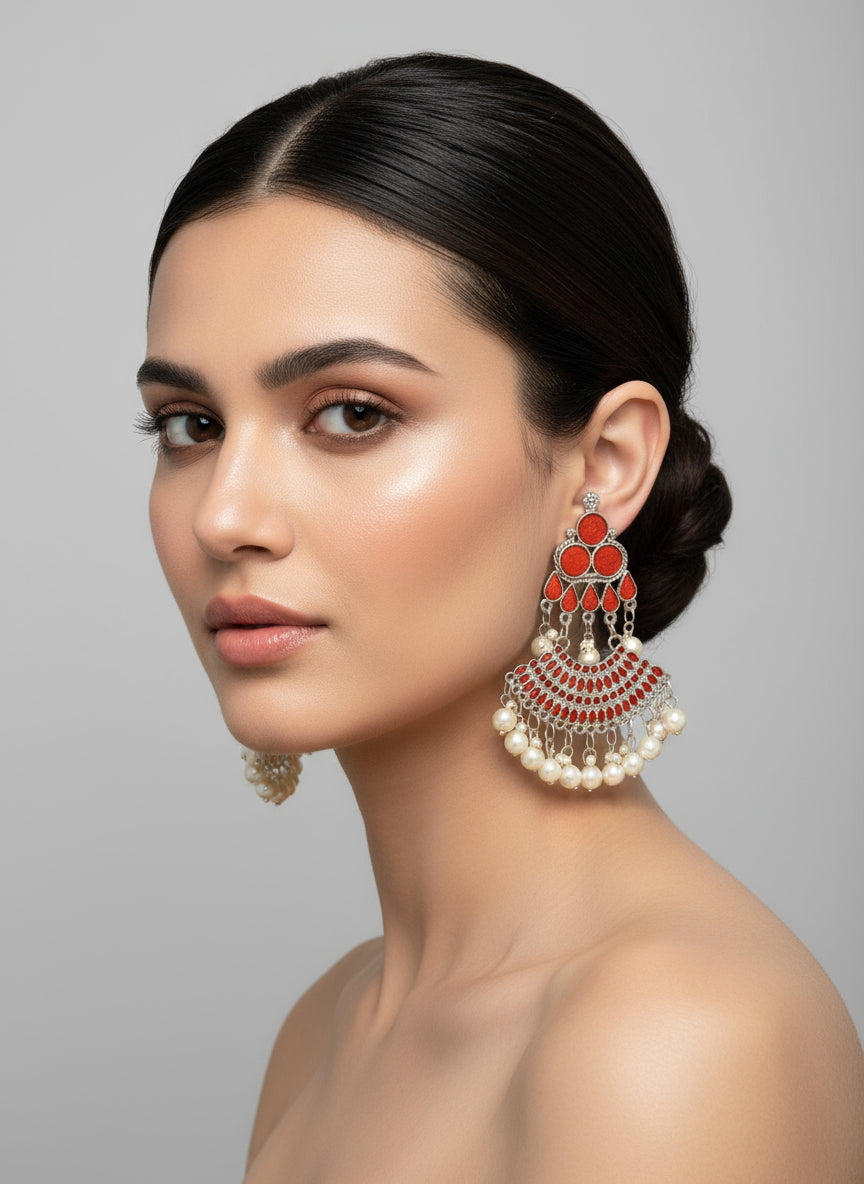 Ornate earrings with orange paint stones and pearl-like beads on a display stand.