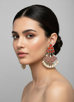 Ornate earrings with orange paint stones and pearl-like beads on a display stand.