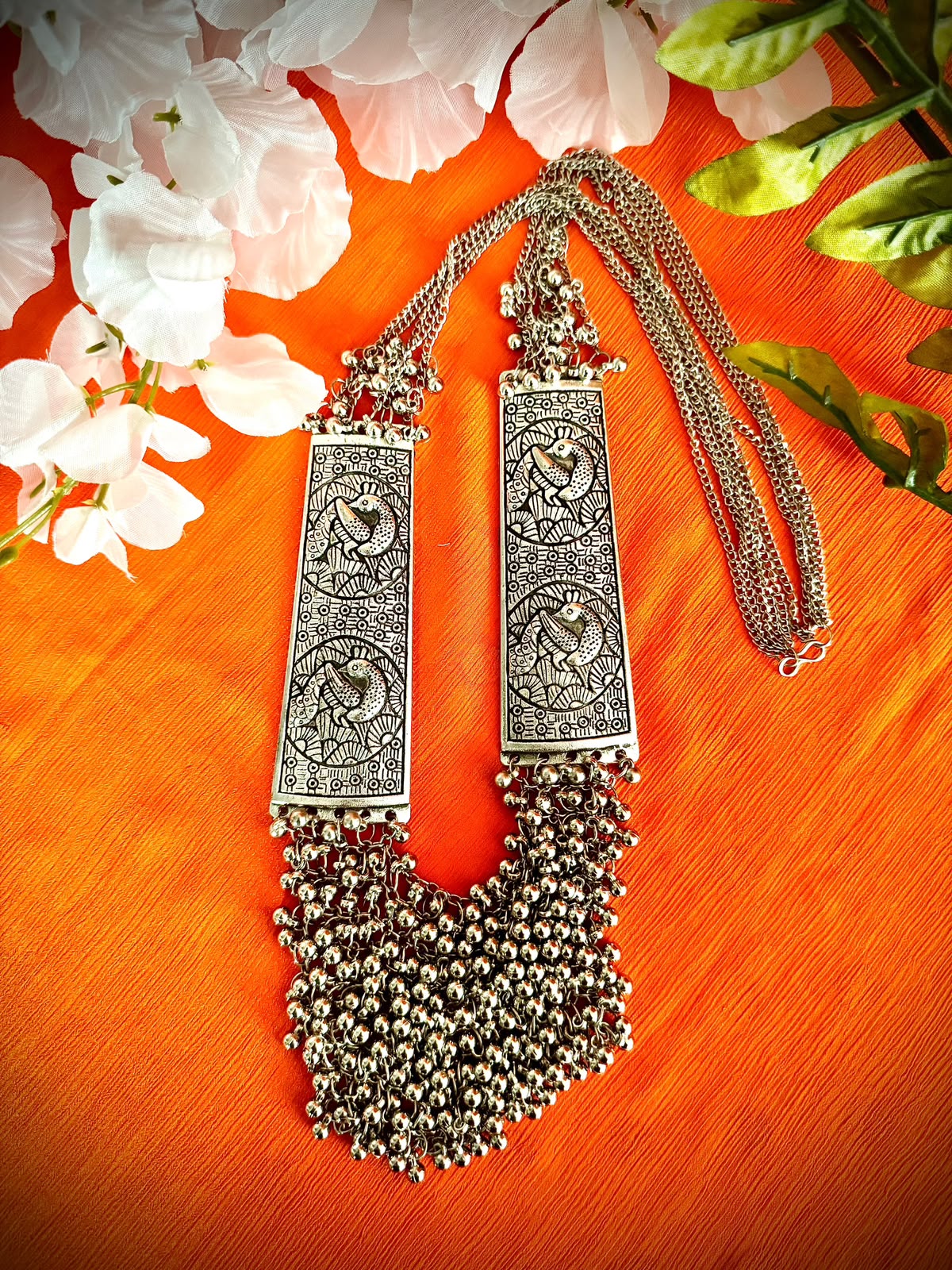 Silver Sonata long mala necklace laid on orange fabric, showing peacock panels, chains and clasp