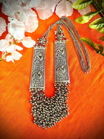 Silver Sonata long mala necklace laid on orange fabric, showing peacock panels, chains and clasp
