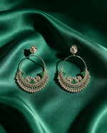 Pair of oxidized silver peacock chandbali hoop earrings with emerald green stone accents and ghungroo fringe — displayed on rich emerald green satin silk, antique silver finish, luxury ethnic jewelry by Famaza Couture.
