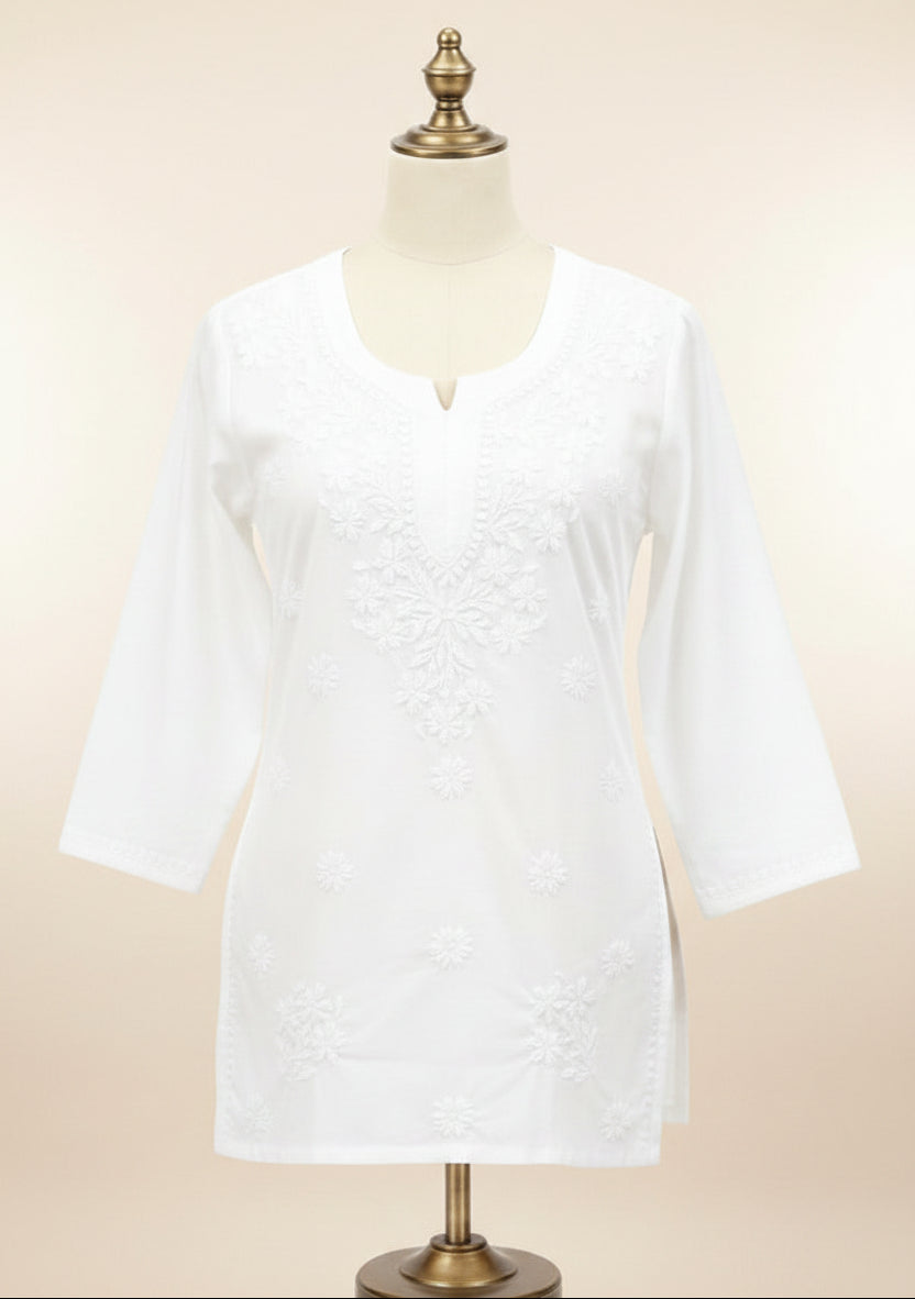 A bright pink tunic top with floral embroidery on the front, displayed on a cream dress form with a gold-colored stand against a white background.