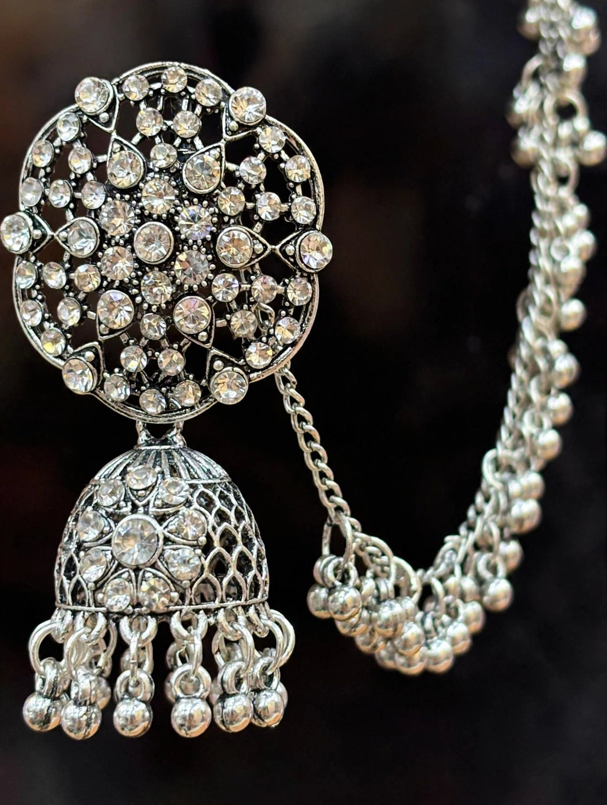 Close-up of a Pakeezah Moonlight jhumka earring showing clear stones, an openwork dome and a beaded Sahara chain.