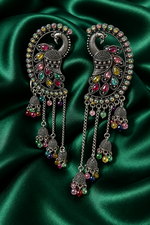 Antique silver peacock meenakari chandbali jhumka earrings with vibrant multicolor gemstone detailing, long chain tassel drops, displayed on rich emerald green satin — Indian Pakistani bridal ethnic jewelry.