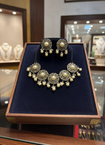 Pair of ornate earrings with pearls on a white stand.