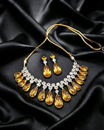 A high-angle flat lay view of a micro gold plated yellow crystal and cubic zirconia choker necklace with matching teardrop earrings displayed on a dark satin background.