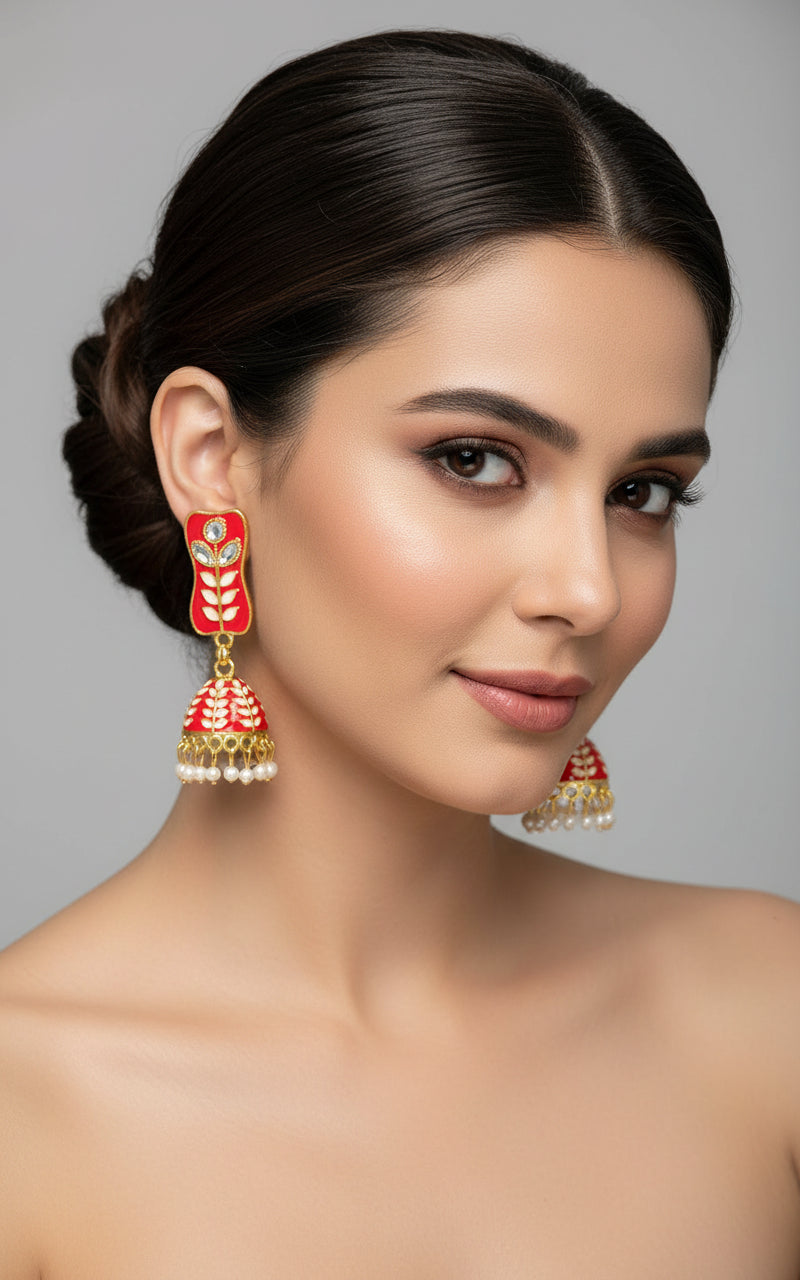 red colour pair of gold-platedMeenakari drop Jhumka earrings displayed on a stand, featuring intricate designs and studded with stones.