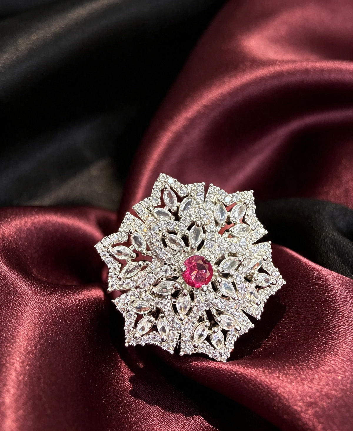 Close-up of Elegant Silver & Pink American Diamond Ring — Luxury Collection by Famaza Couture, snowflake halo design with marquise-cut stones and vibrant pink center, resting on burgundy satin fabric.