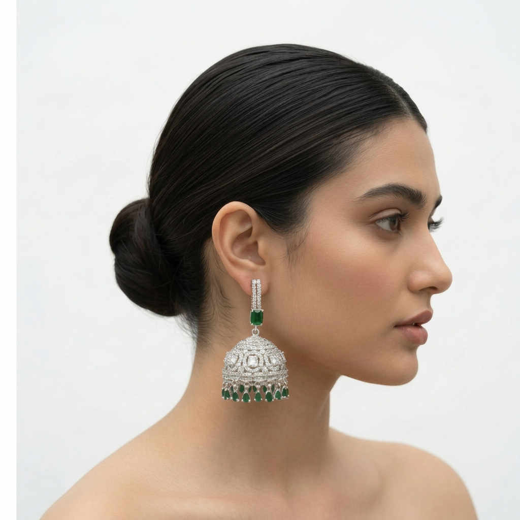 Silver-tone American diamond jhumka earrings with green stone accents and teardrop dangles on a black stand.