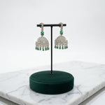 Model wearing a silver-tone green stone jhumka earring, with labelled measurements of 5.5 cm length, 5 cm dome width and 0.5 cm top width.