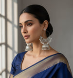 Silver earrings with pearl accents held by a hand against a blurred natural background