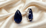 Navy blue teardrop crystal studs on cream fabric, showing the silver-tone setting and post from the side.