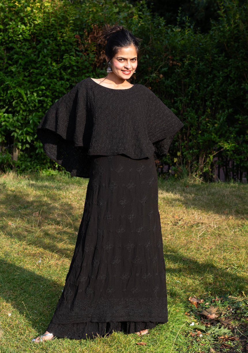 A woman wearing a black viscose capelet dress with traditional Chikankari handwork embroidery.