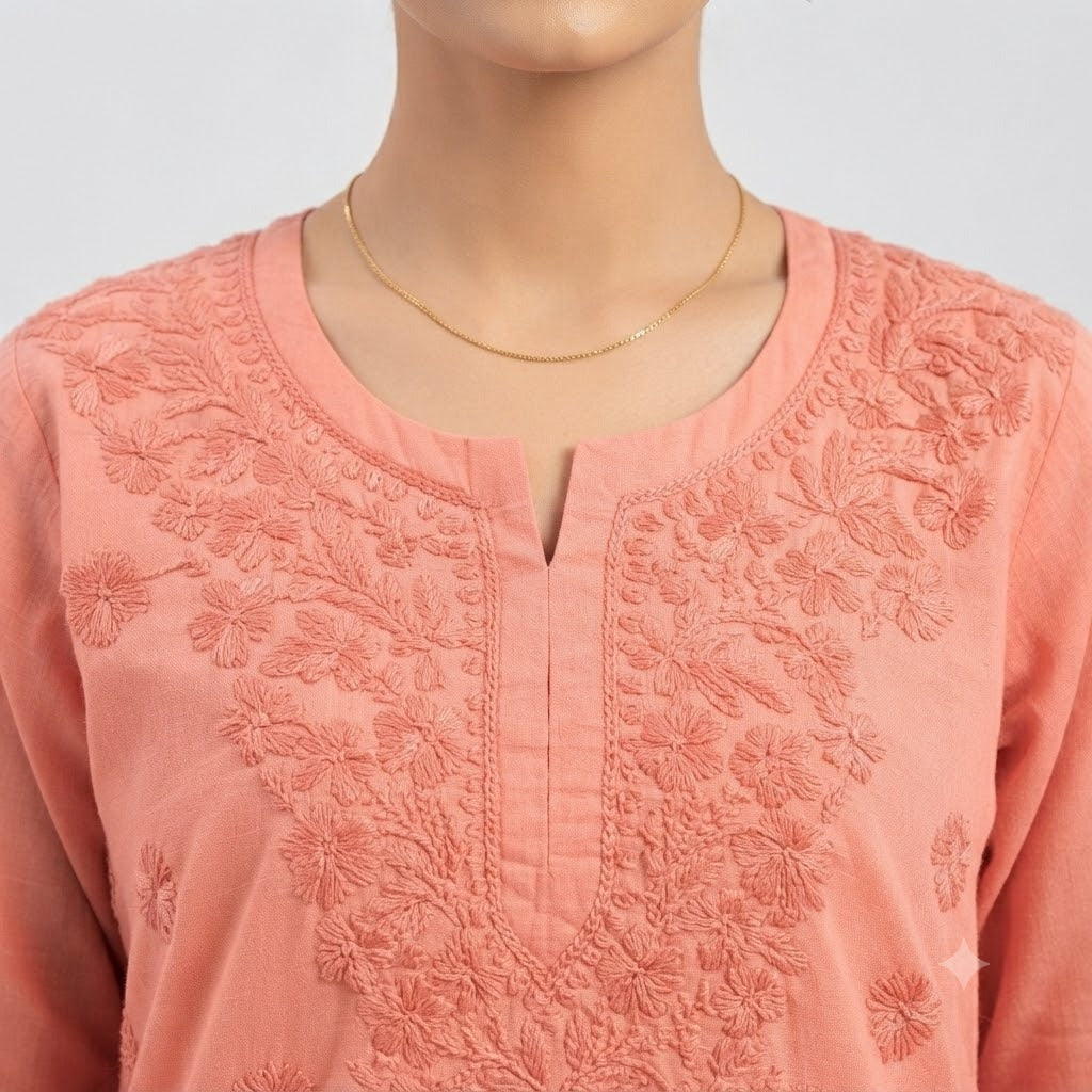 A close-up of a peach-pink embroidered kurta with a split neckline, shown on a mannequin torso with a delicate gold chain necklace.