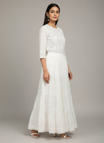 White lace dress held up against a wooden floor with books in the background