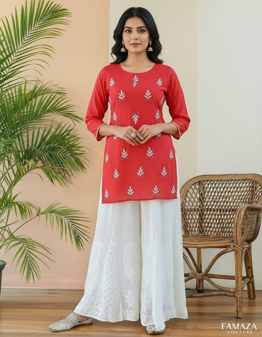 White embroidered pants with a yellow top against a peach wall with green leaves.