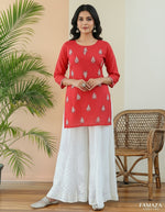 White embroidered pants with a yellow top against a peach wall with green leaves.