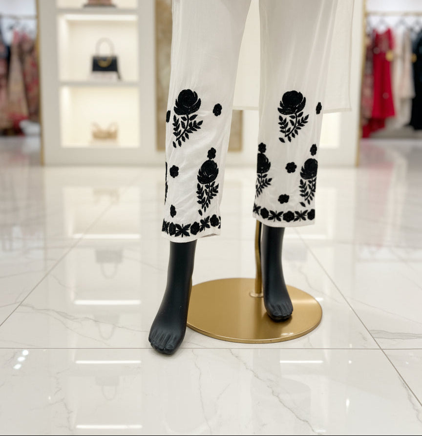 Mannequin wearing a white dress with black floral patterns on a herringbone floor.