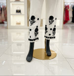 Mannequin wearing a white dress with black floral patterns on a herringbone floor.