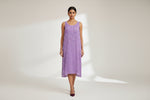 A lavender sleeveless mesh dress with floral embroidery on the bodice, hanging on a white hanger in front of a store display filled with jewelry.