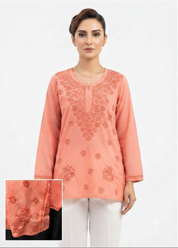A woman modeling a peach-colored long-sleeve kurta with floral embroidery on the chest and scattered motifs below, paired with white pants against a plain white background. An inset detail box in the bottom-left corner shows a close-up of the embroidery texture.