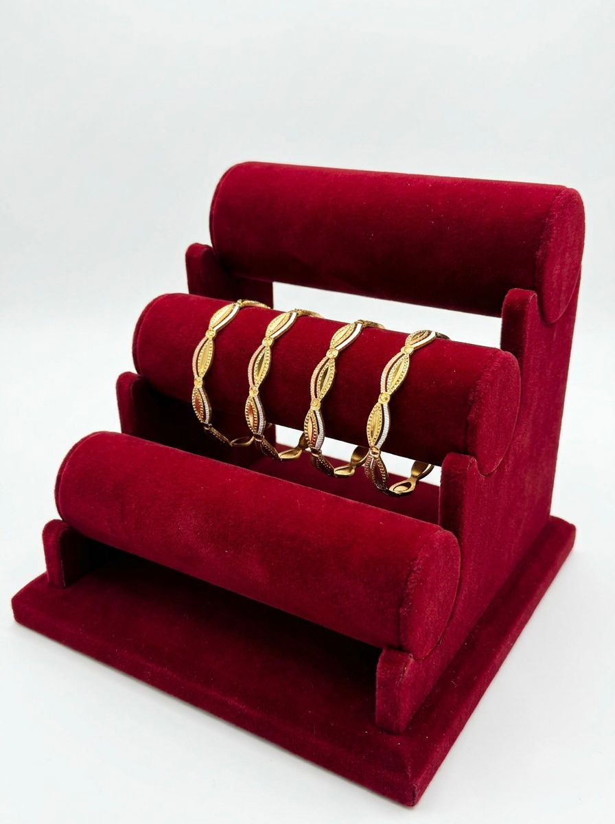 A set of four three-tone micro gold-plated copper bangles featuring an intricate floral lattice and scalloped eyelet design in yellow, white, and pink gold finishes, displayed on a tiered red velvet jewelry stand.