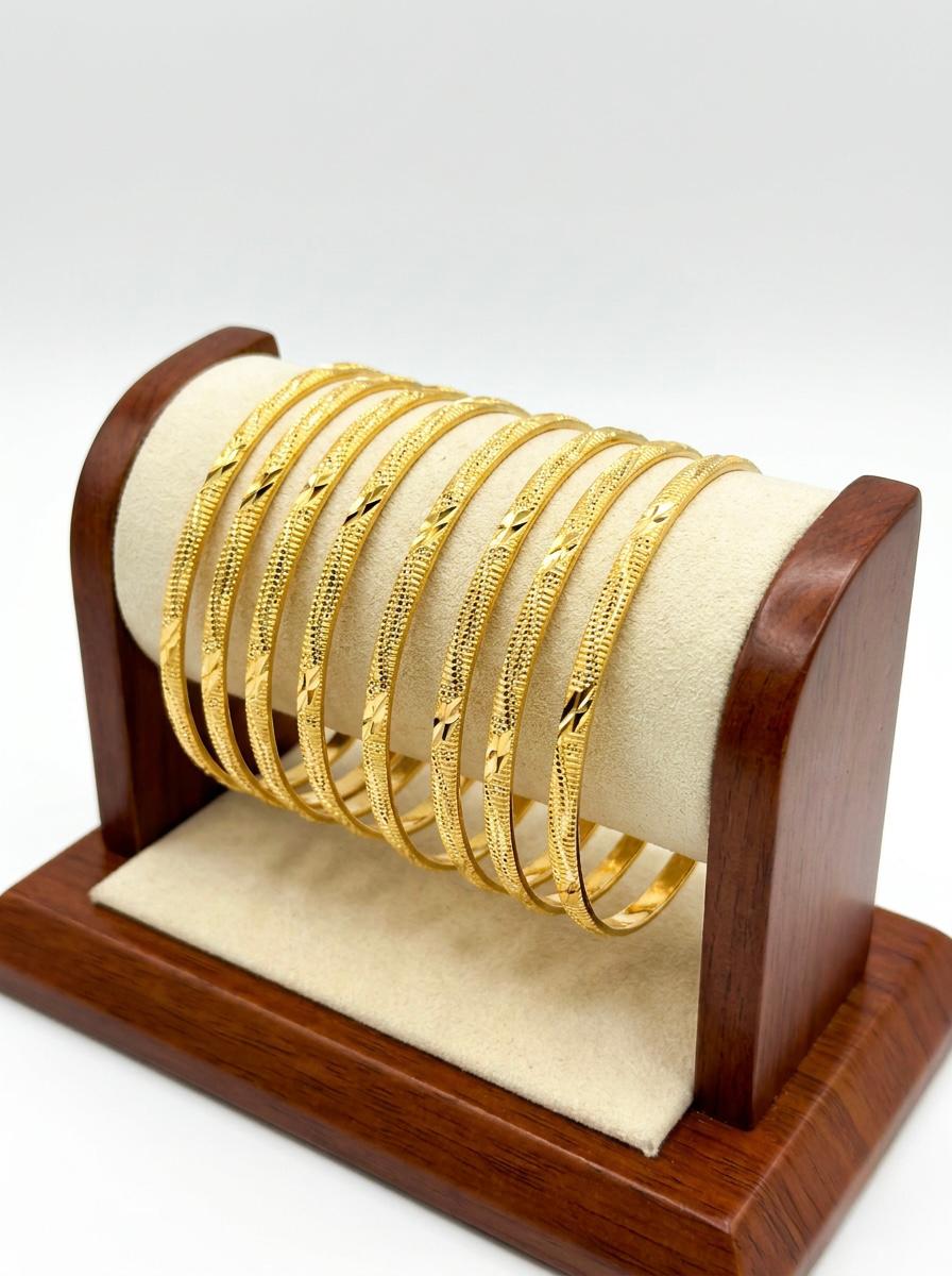A set of eight micro gold-plated copper bangles featuring an intricate twisted rope and wavy vine texture, displayed on a posh wooden and cream suede jewelry stand against a white background.