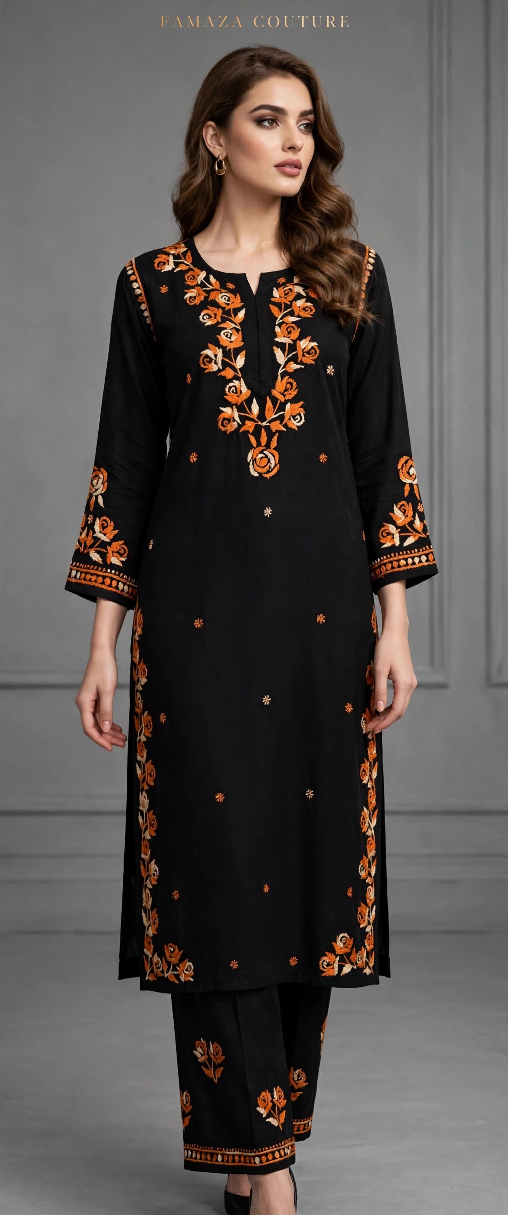 A woman modeling a black three-piece kurta set with orange and gold floral embroidery, featuring a long tunic, matching pants, and embroidered cuffs, set against a gray studio background.