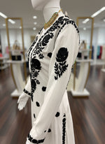 White dress with black floral embroidery on a mannequin against a white background