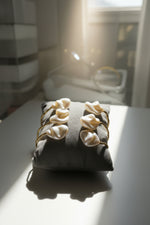 A 14k gold-plated brass cuff with iridescent white Mother of Pearl inlay resting elegantly on a plush velvet jewelry cushion.