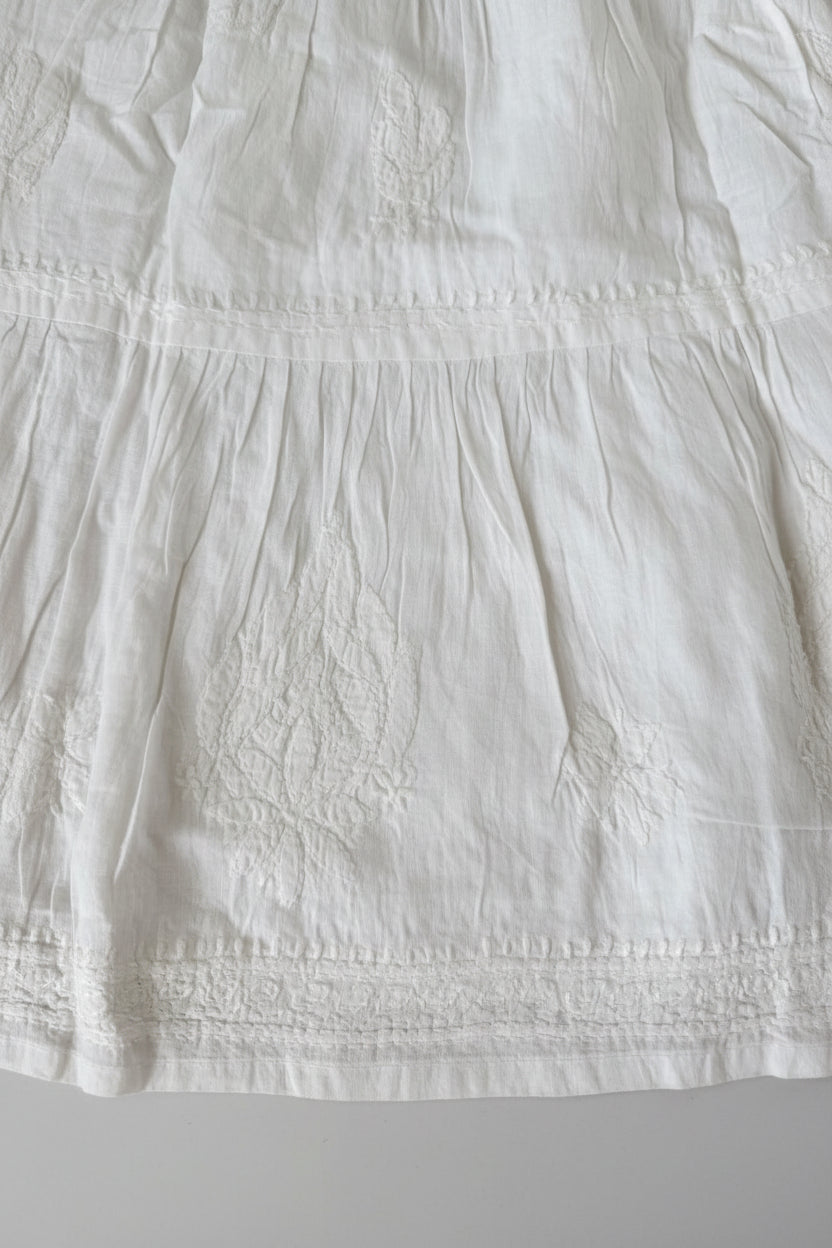 A Close-up of a white embroidered fabric garment, showing textured embroidery and gathered seams.