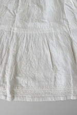 A Close-up of a white embroidered fabric garment, showing textured embroidery and gathered seams.