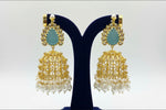 Gold and pearl earrings on a black stand with a white background.