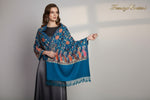 A Teal blue pashmina scarf with Kashmiri Aari embroidery in a floral pattern, featuring tassels on the ends.
