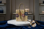 A beige floral handcrafted tote bag with glass beads embroidered on it, displayed on a wooden surface.