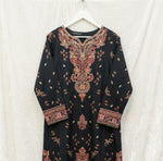 A black long-sleeve kurta with intricate red, gold, and beige embroidery concentrated on the yoke and cuffs, laid flat on a patterned fabric surface.
