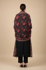 A black long rear view of this kurta with red and pink floral embroidery on the sleeves cuff and a red printed dupatta is, displayed on a hanger in a Famaza Couture store.