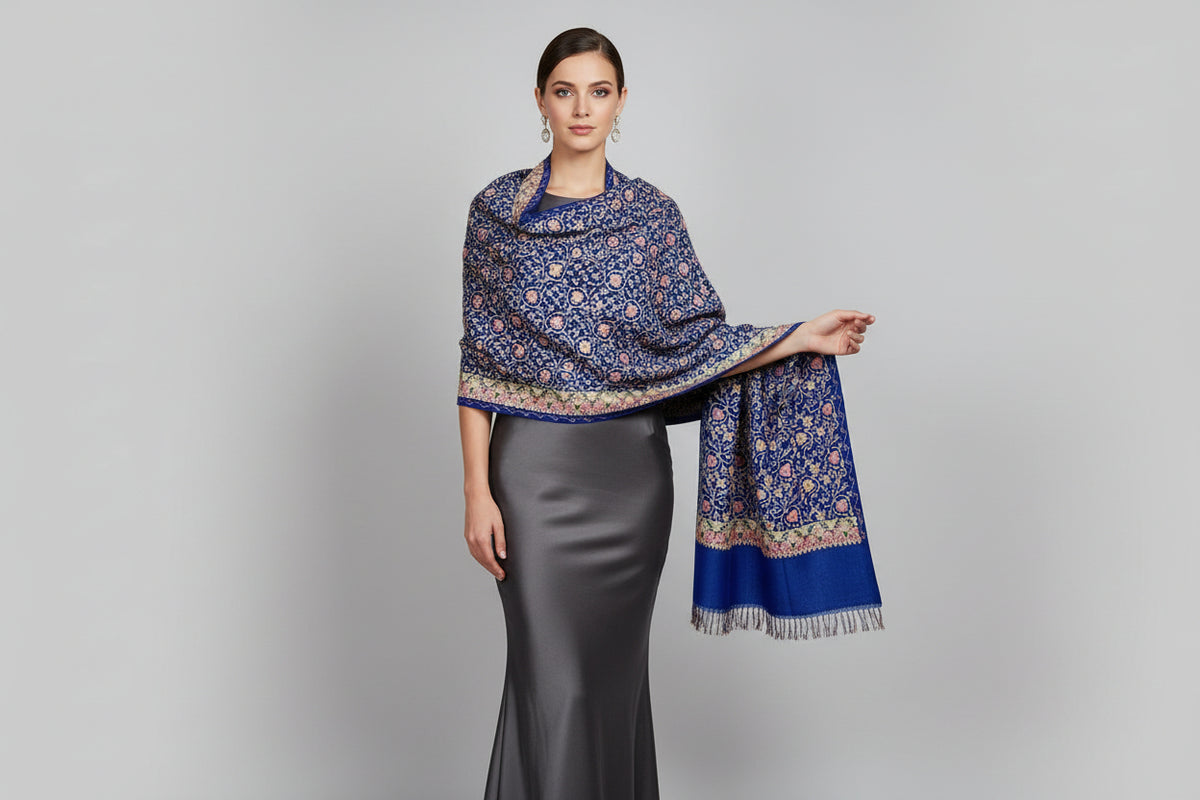 A blue Kashmiri embroidered pashmina scarf with maple leaf motifs and tassels on the ends, displayed on a wooden surface.