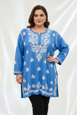 A woman modeling a blue long-sleeve kurta with white floral embroidery, paired with black pants, against a draped white fabric background.