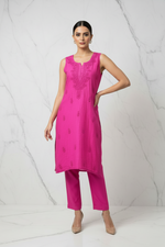 A woman modeling a bright pink kurta and matching trouser set against a white marble-patterned studio backdrop.