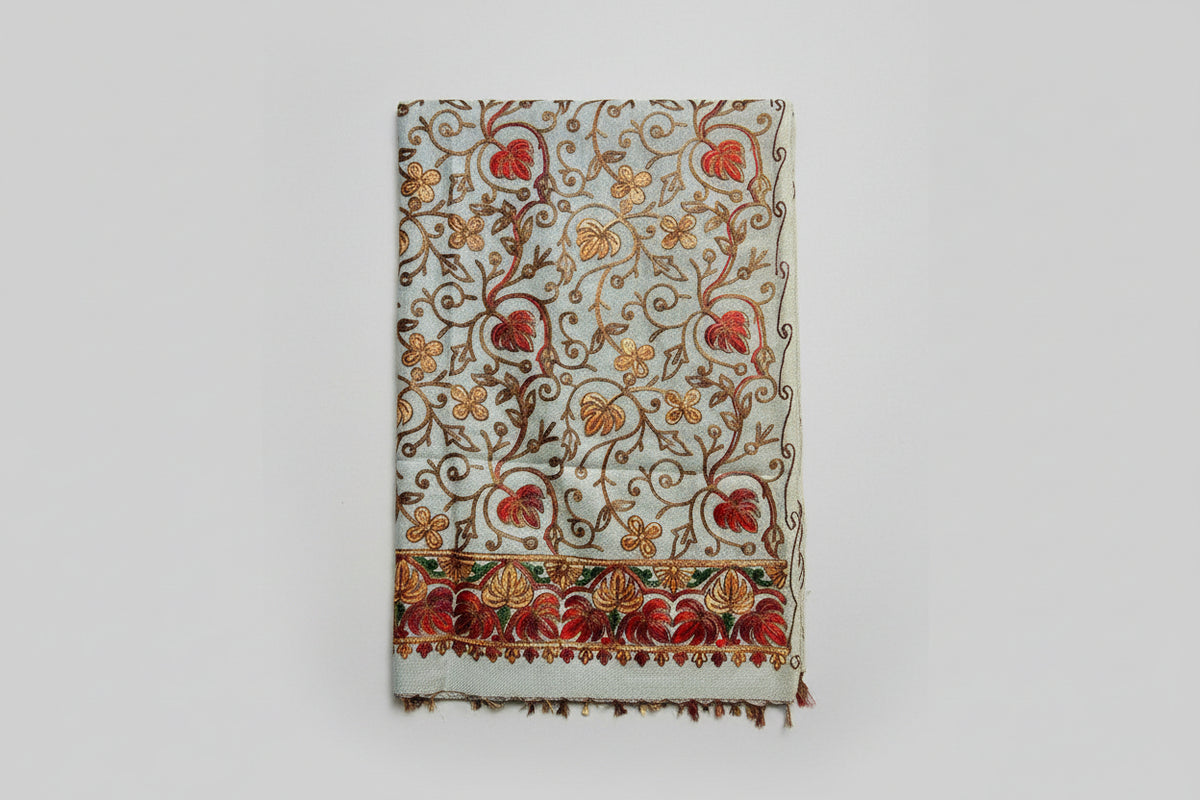 A close-up of White base colour Kashmiri embroidered pashmina scarf with maple leaf motifs and tassels on the ends, displayed on a wooden surface.