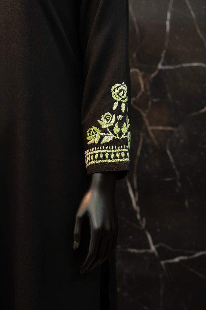 A close-up of a black sleeve featuring detailed green and white floral embroidery with rose motifs and a decorative border.