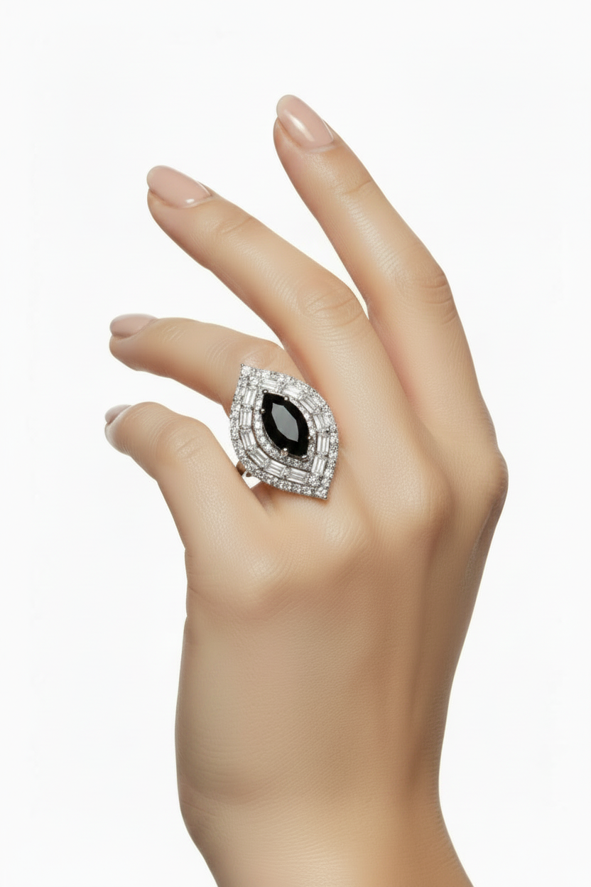 A hand wearing a large ring with a marquise-shaped black center stone surrounded by a halo of small clear stones on a white background.