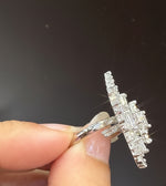 A close-up of a hand holding a silver-toned ring with a large, multi-stone baguette cluster setting.