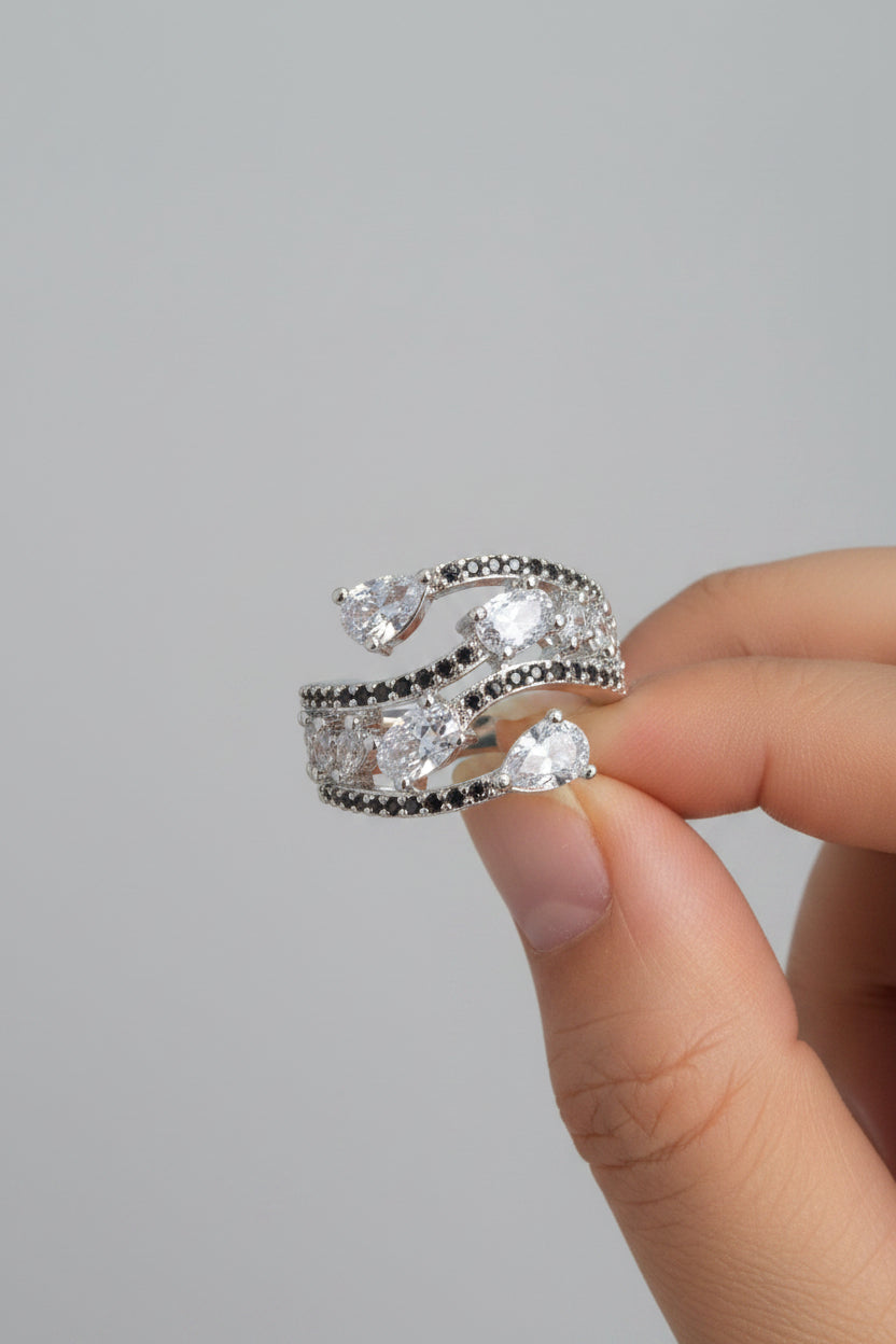 A close-up of a hand wearing a silver-toned wrap ring adorned with clear teardrop and round-cut stones.