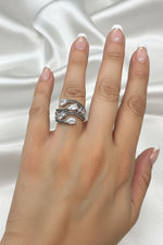 A close-up of a hand wearing a silver-toned wrap ring with clear teardrop-shaped stones and small dark pavé accents, set against a black background.