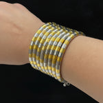 A close-up of a person's wrist wearing a stack of wide metallic bracelets made of alternating yellow-gold and silver-toned rectangular links.